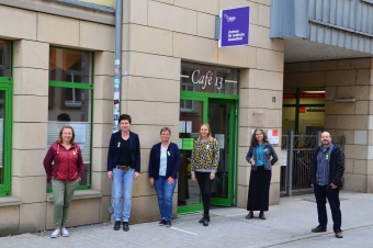 5 Frauen und 1 Mann stehen nebeneinander vor einem Café und tragen alle eine Grüne Schleife am Pullover
