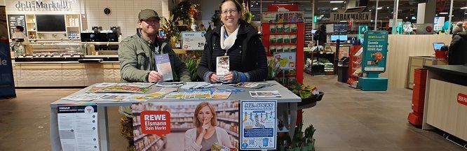 Frau und Mann an einem Infotisch im Supermarkt